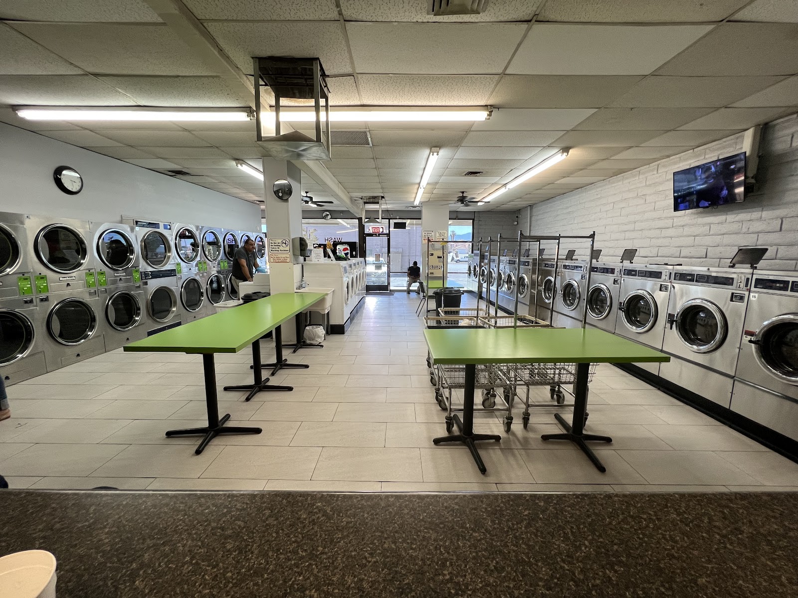 Bright clean laundromat interior with green folding tables and rows of washers and dryers