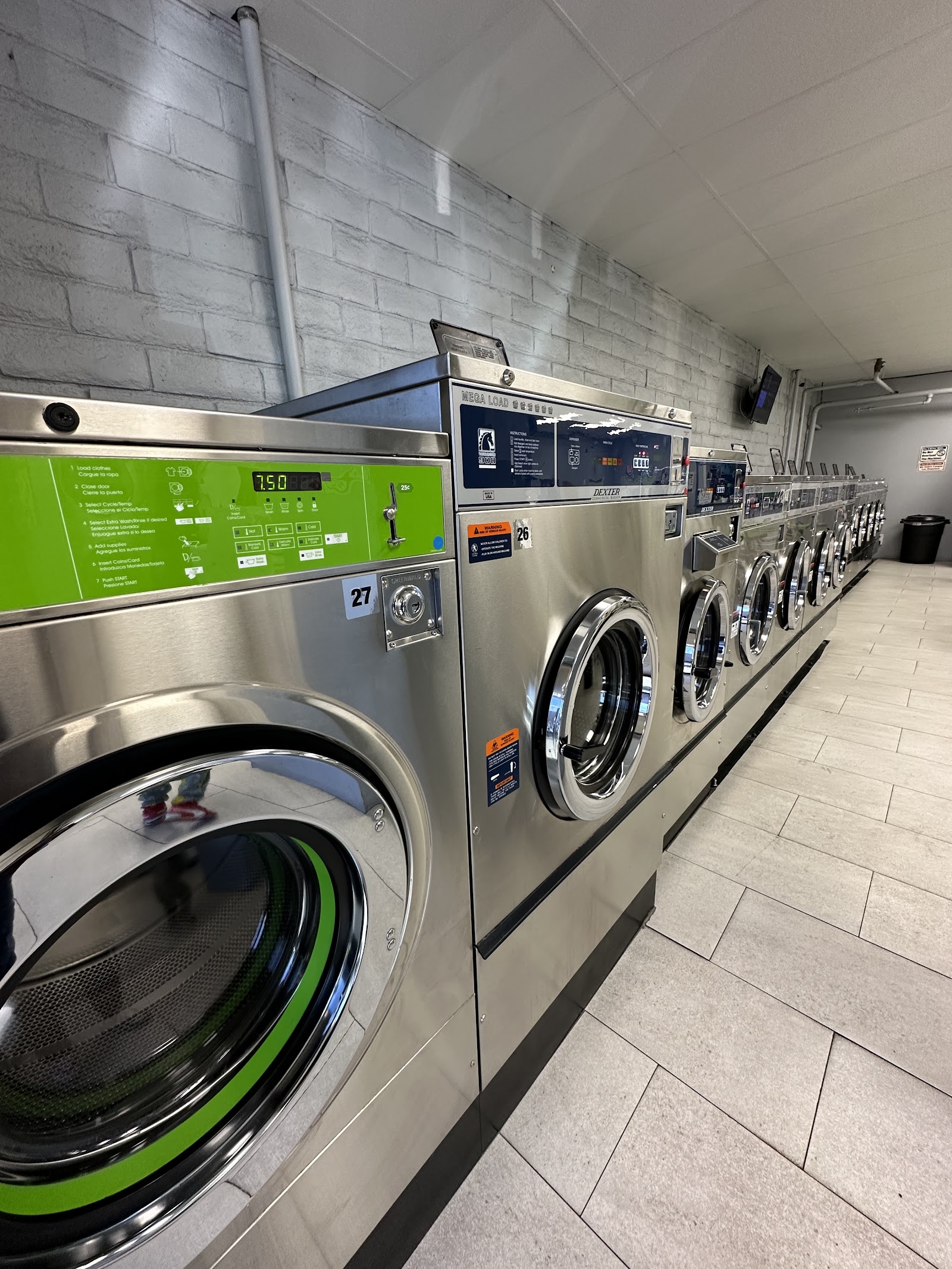 Row of stainless steel Dexter front-load commercial washers with green control panels